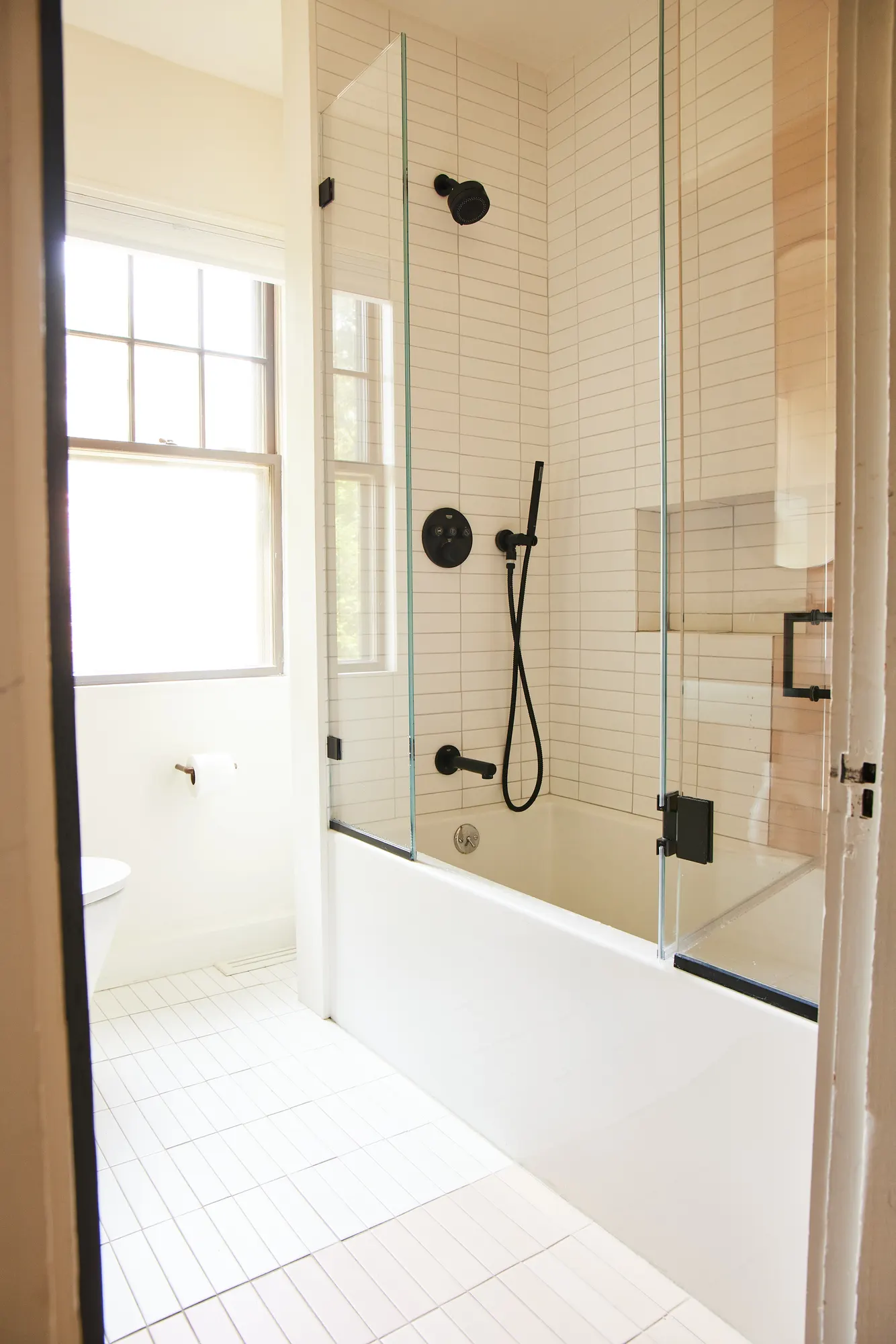 A tub behind a glass screen with black fittings, beside a window.
