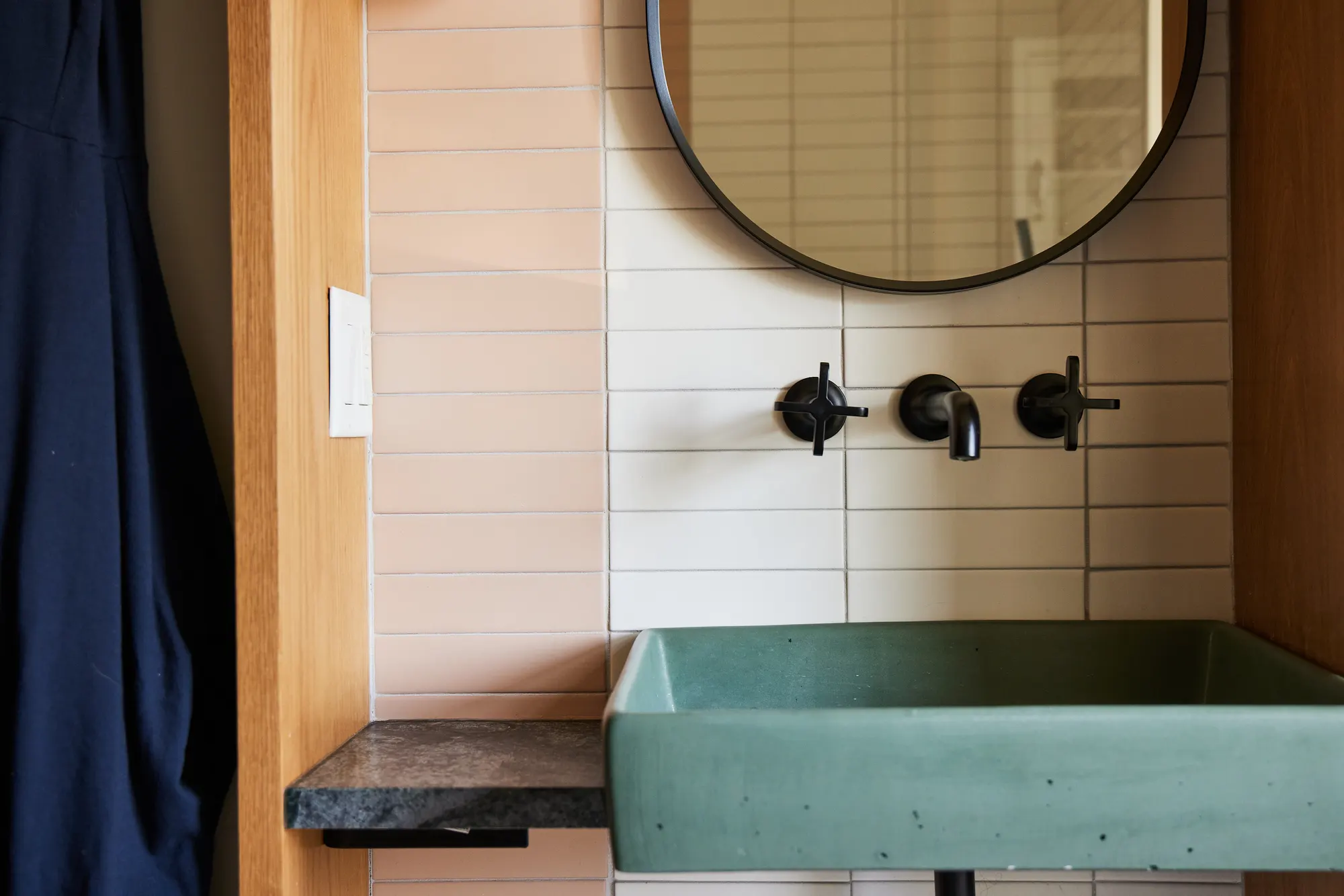 The green trough basin across the tiled wall, with black taps and a stone shelf.