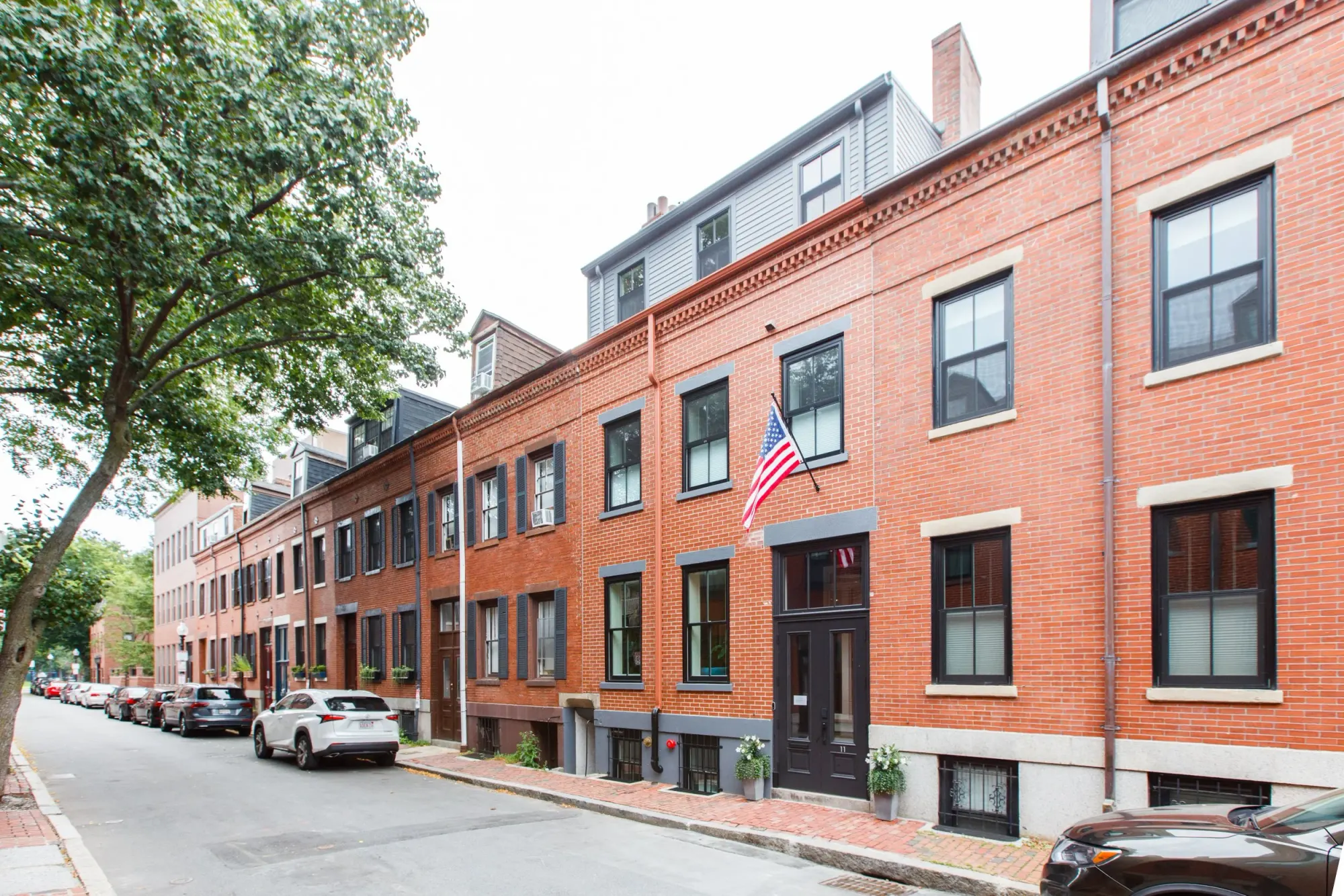 A row of brick rowhouses along the street, with cars parked in front.