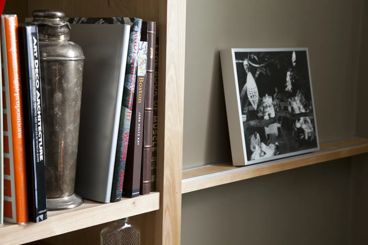Books and a steel cocktail shaker on a shelf, beside a framed photograph on a picture ledge.