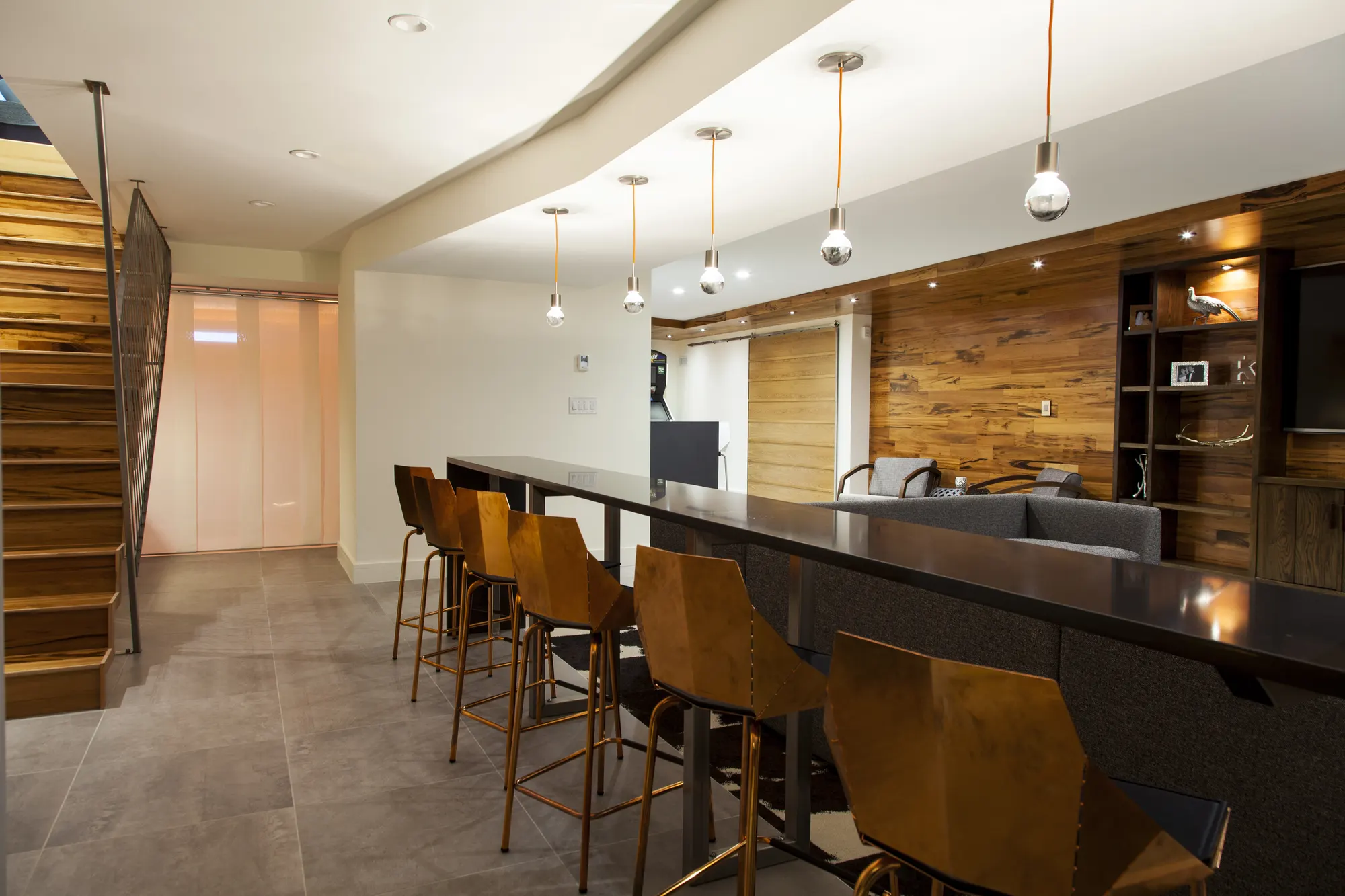 Leather-seated stools along a long dark bar under a curved soffit and pendants, with the stair at the left.