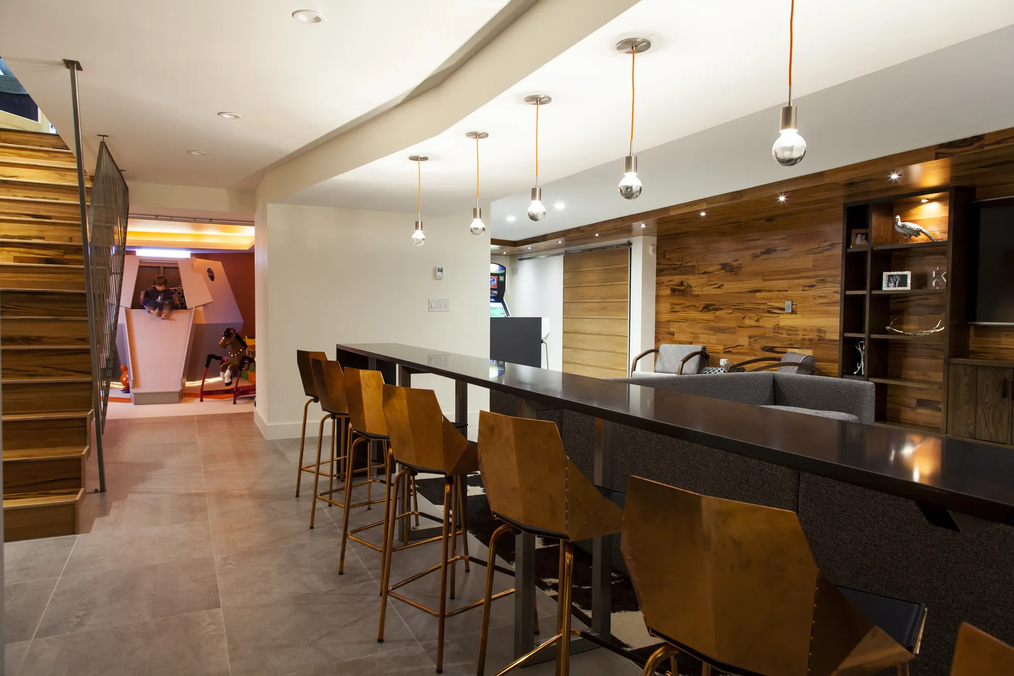 The same bar and stools, with the lit playroom visible through the doorway beyond.