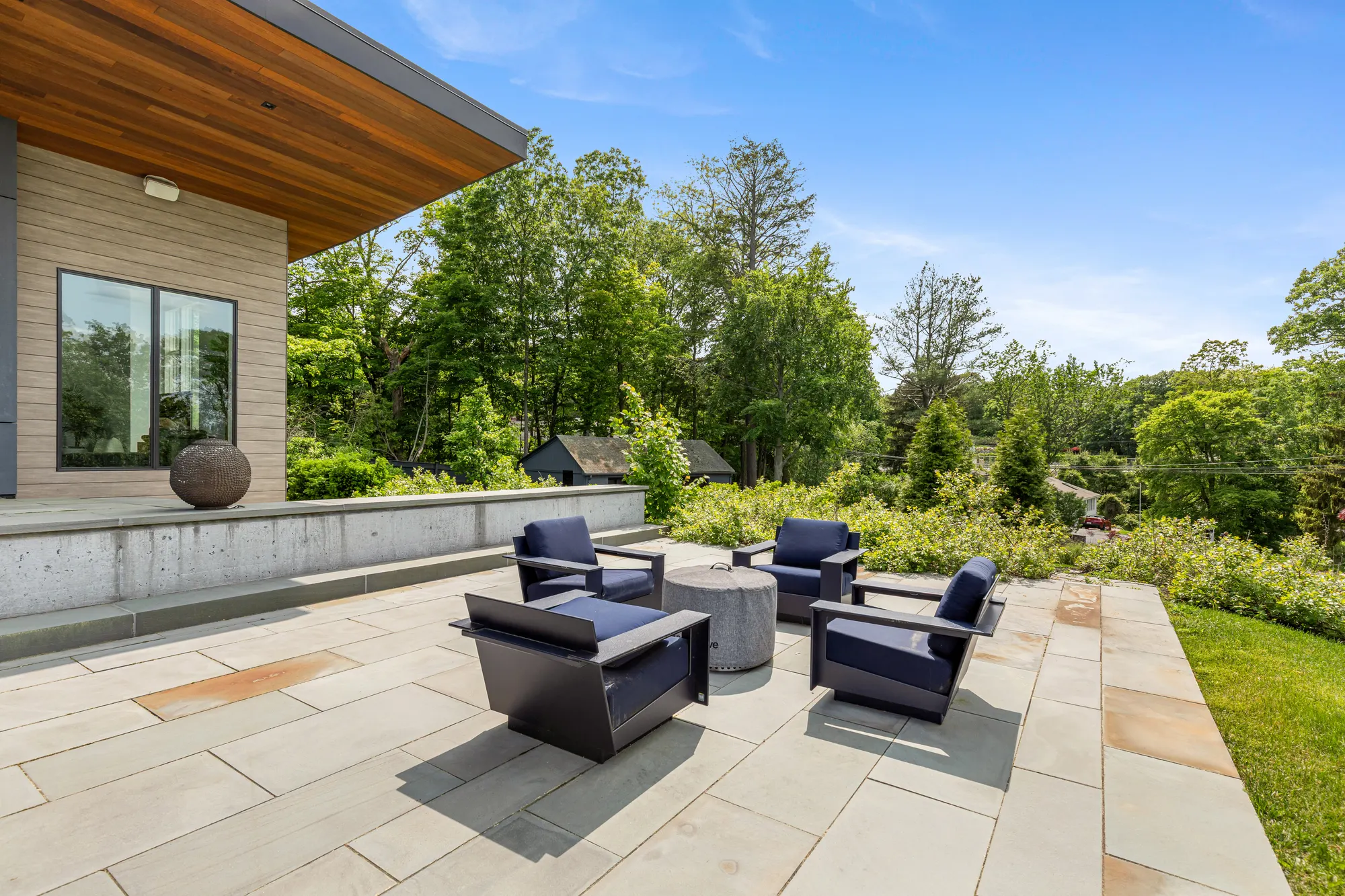 Lounge chairs around a low table on the terrace, with trees beyond the low wall.