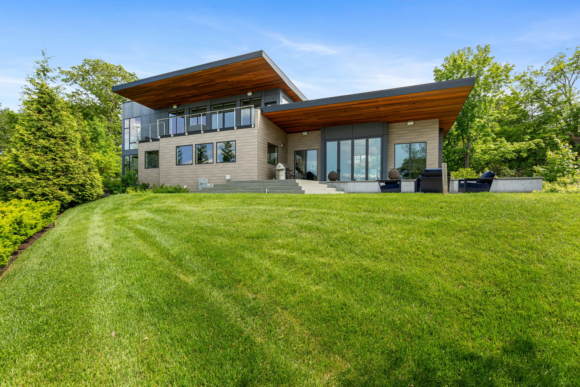The house across a wide mown lawn, its two roofs overhanging the upper floor.