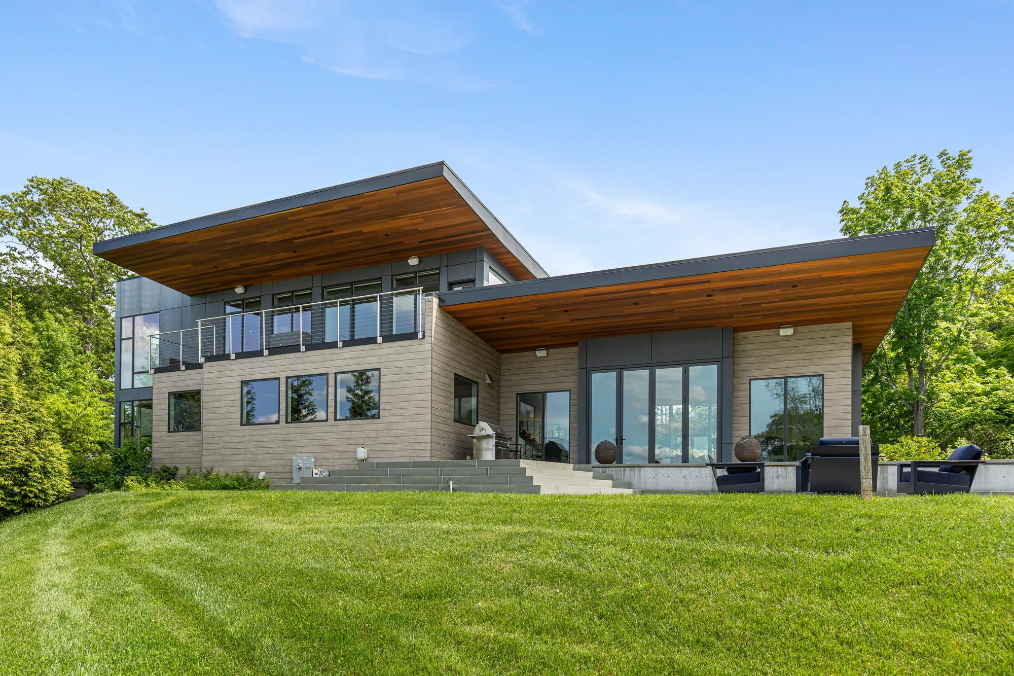 The garden front with its two overhanging roofs, the terrace and chairs at the top of the lawn.