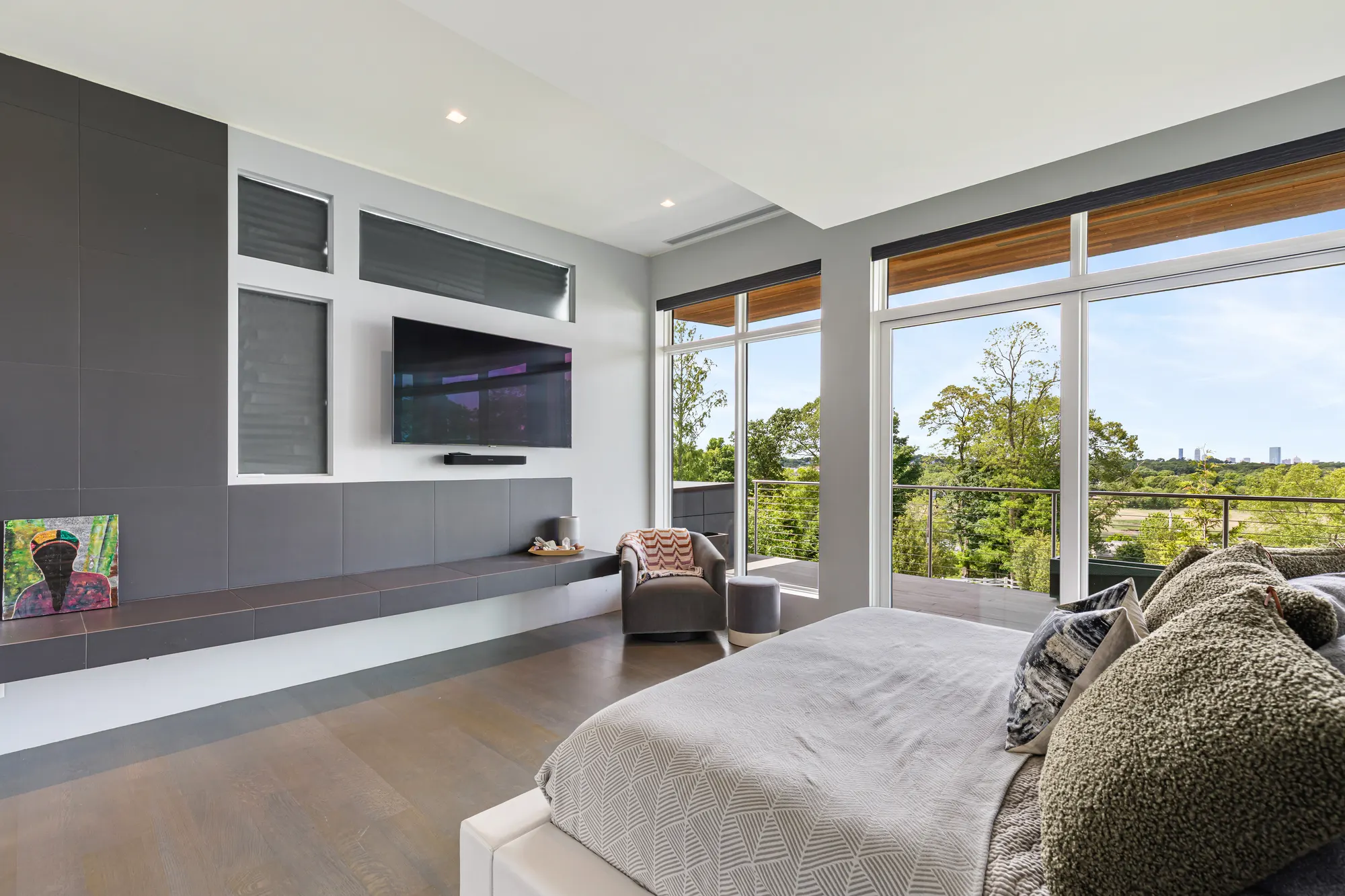 A bed facing a wall with a television and long window seat, with glazing wrapping the corner beyond.