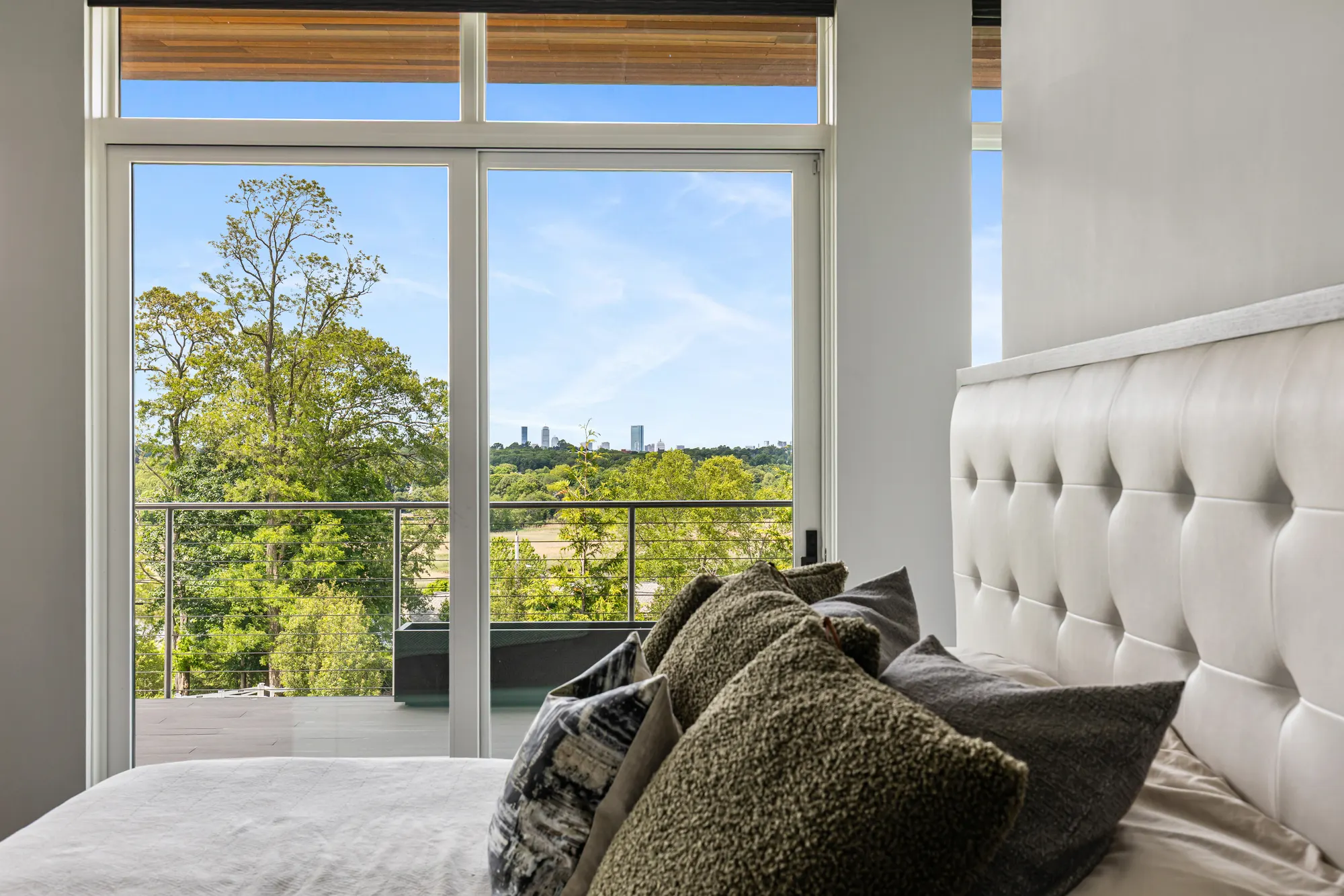 Tall glass doors from the bedroom onto a railed deck, with trees and the city skyline beyond.