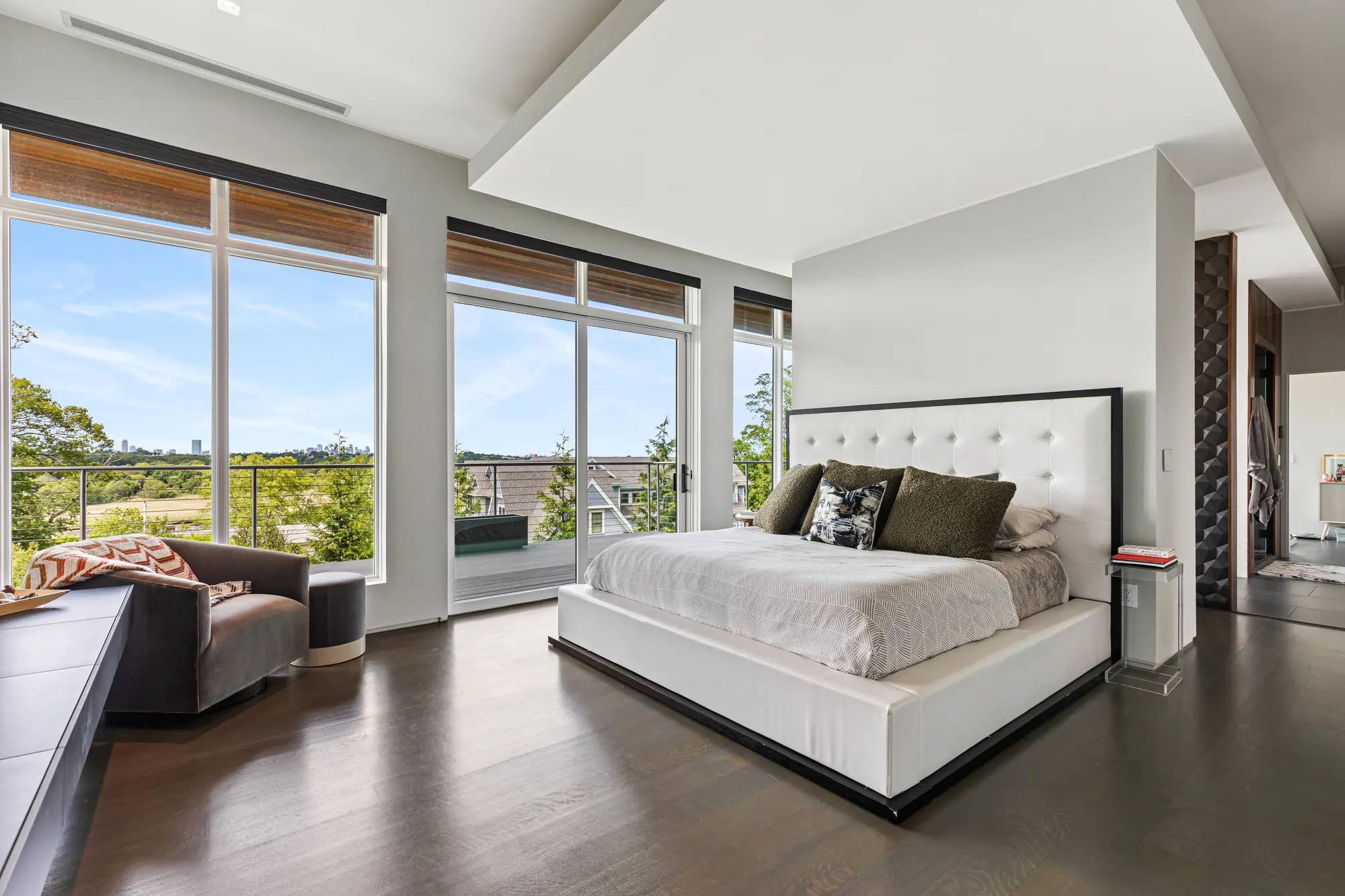 A white upholstered bed on a dark wood floor, with windows along two walls.
