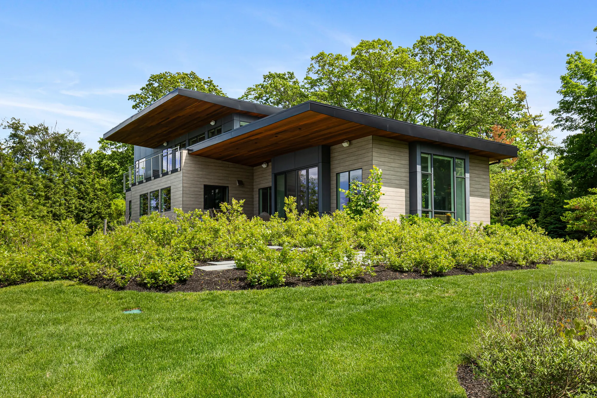 The house above a broad bed of planting, under its two overhanging roofs.