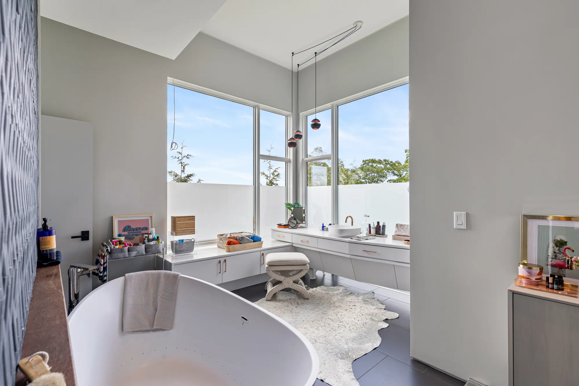 A freestanding tub on the dark floor, with a long vanity under the windows beyond.