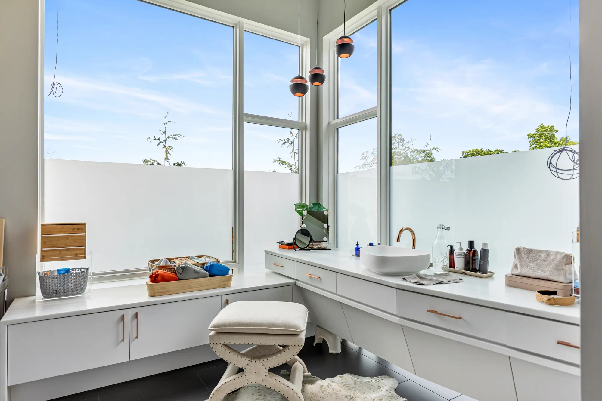 A white vanity with a bowl basin along a corner of tall windows, frosted below, with copper pendant lights.