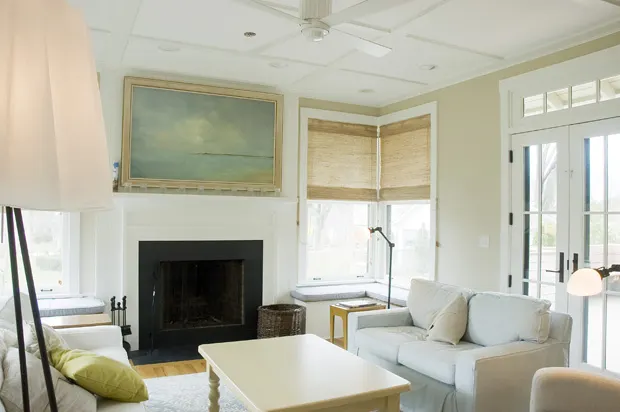 A white fireplace under a seascape painting, with French doors to the side.
