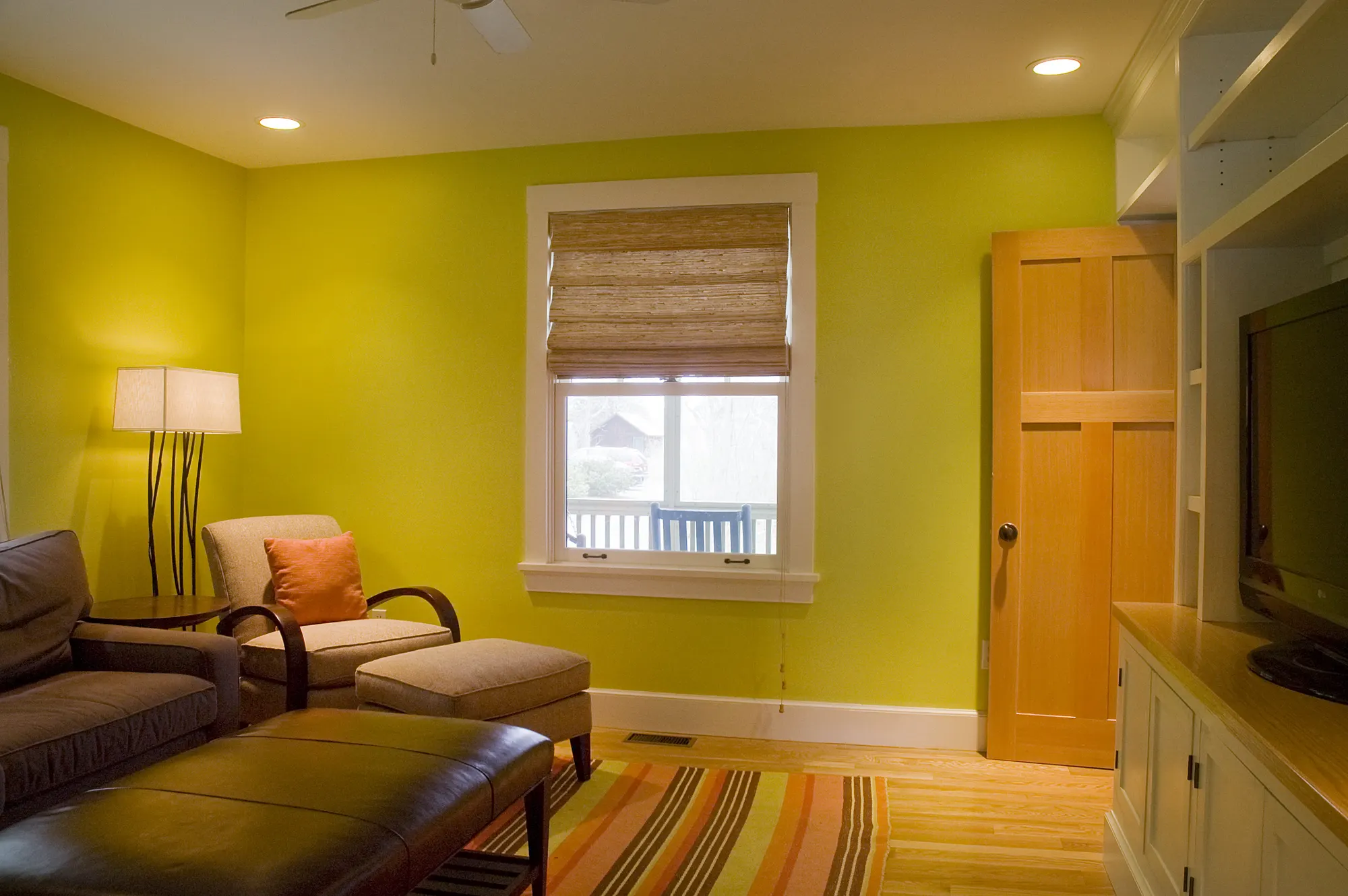 A leather sofa and armchair against a bright yellow wall, with a striped rug.