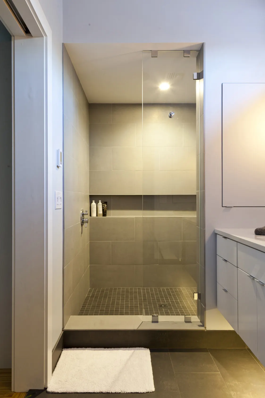 A glass-walled shower in grey tile, with a long niche across the back wall.
