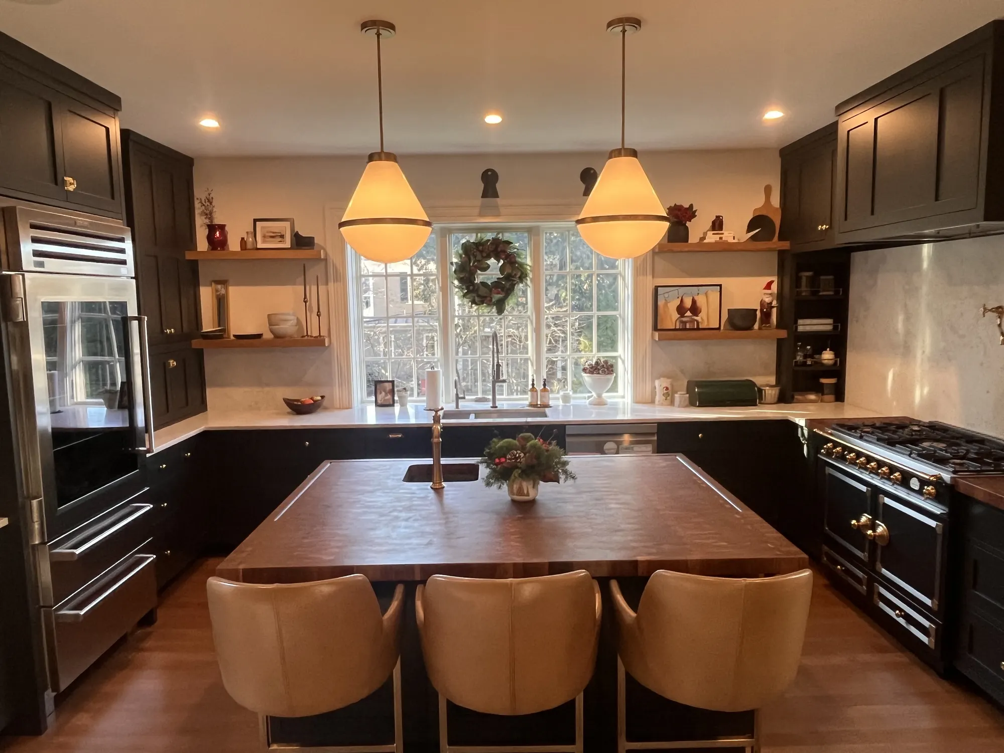 The Milton Kitchen: a walnut-topped island with leather stools under two glass pendants, dark cabinetry beyond