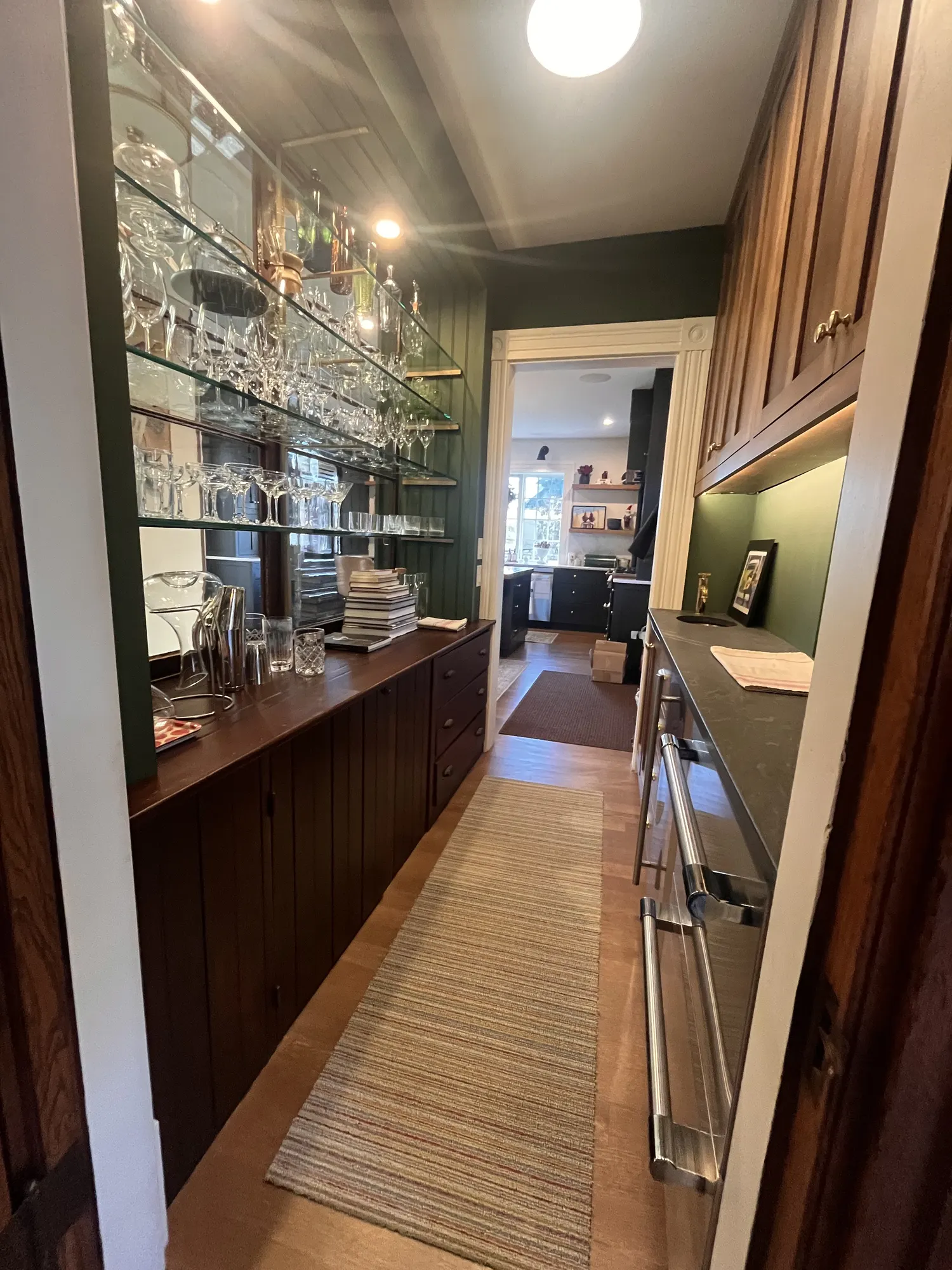 Glass shelves of stemware over walnut cabinets, a runner down the length of the pantry.