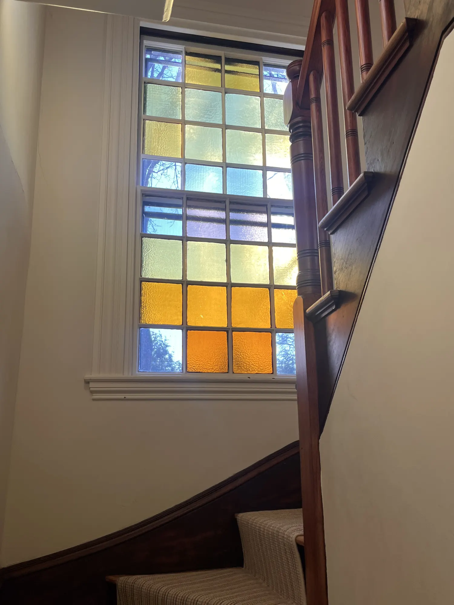 A tall window of yellow and blue stained glass beside the turn of the stair.