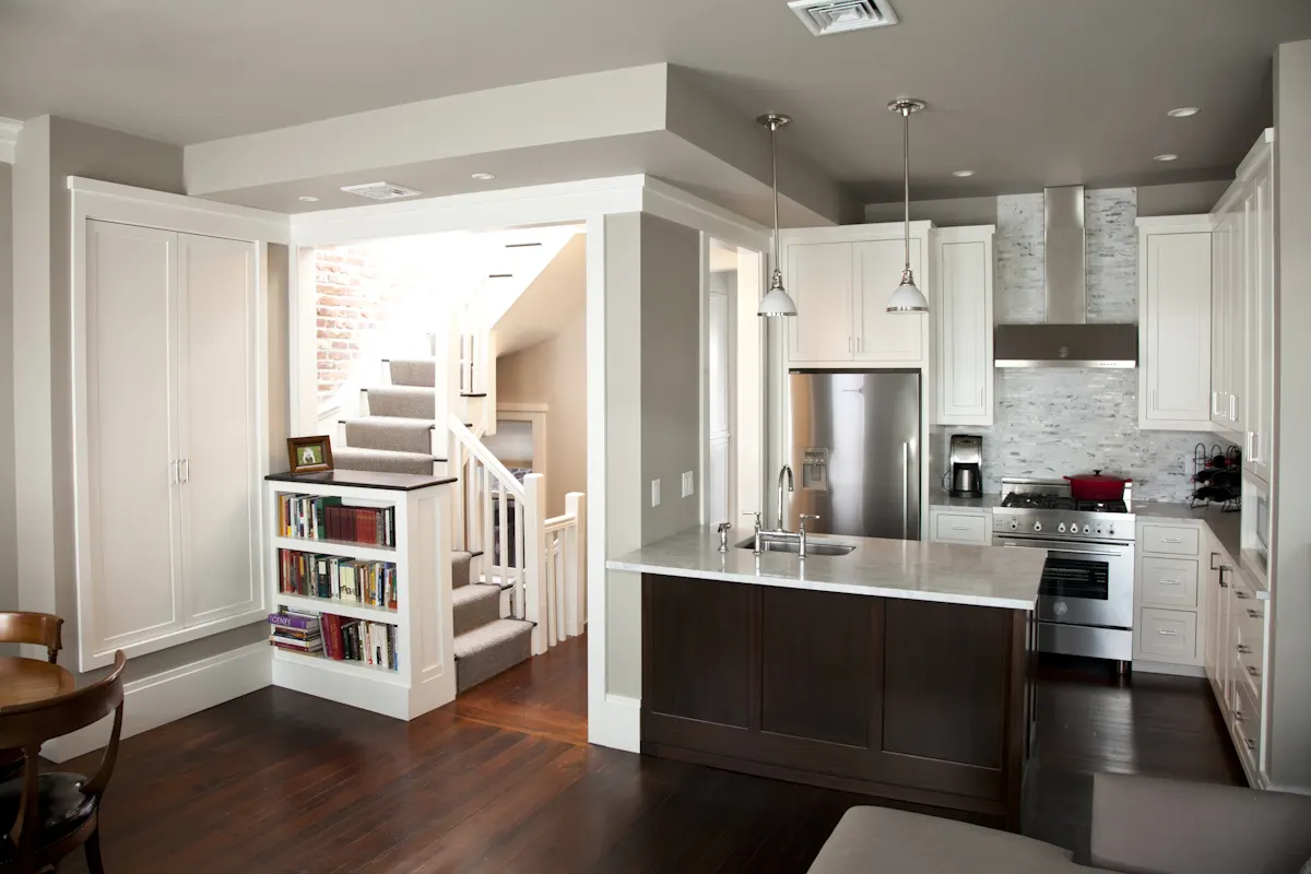 Montgomery Street: a kitchen with white cabinets and a dark island, and a stair with built-in bookshelves beyond
