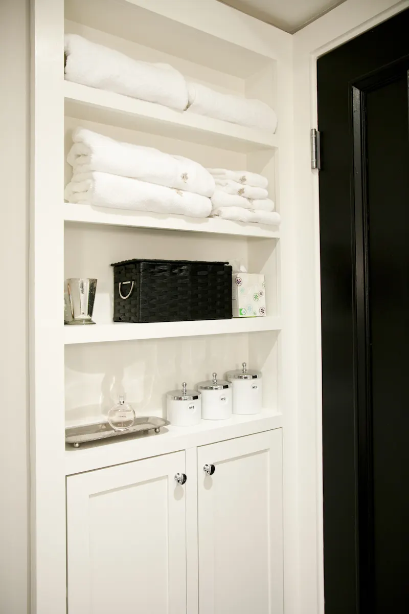 Built-in white shelves of folded towels and baskets beside a black door.