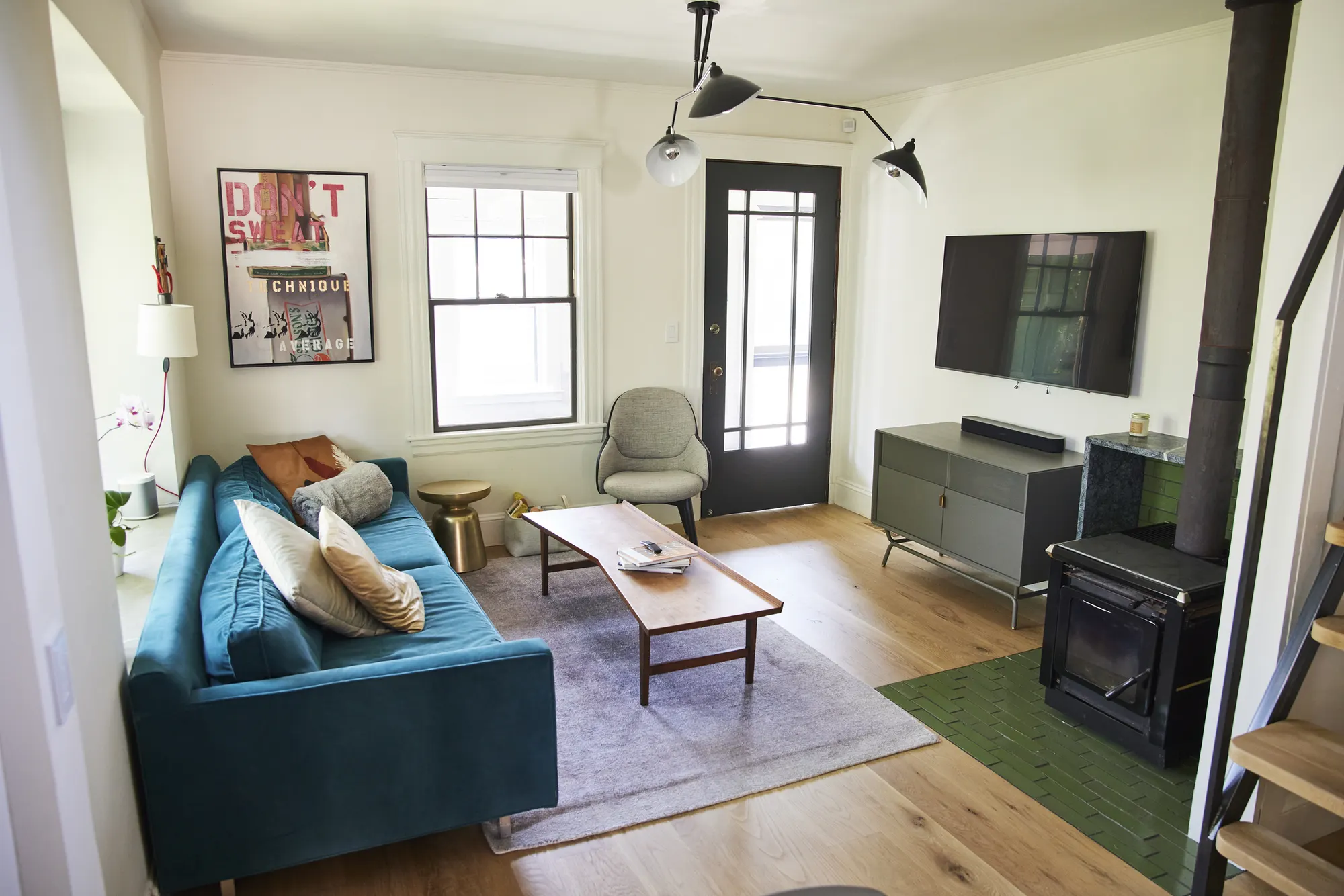 A teal sofa and coffee table facing a television, with the stove on green tile in the corner.