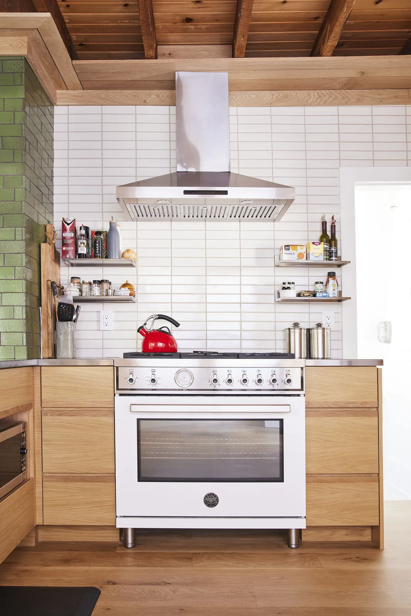 A white range under a steel hood, with white tile carried up behind it and open shelving either side.
