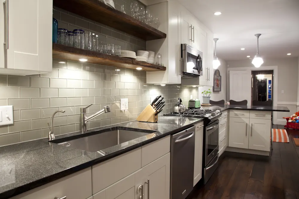 Sullivan Kitchen: a galley kitchen with grey subway tile, dark counters and open timber shelves, a hall beyond