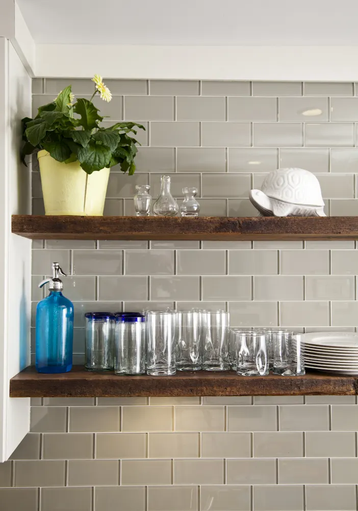 Reclaimed timber shelves of glassware against grey subway tile.
