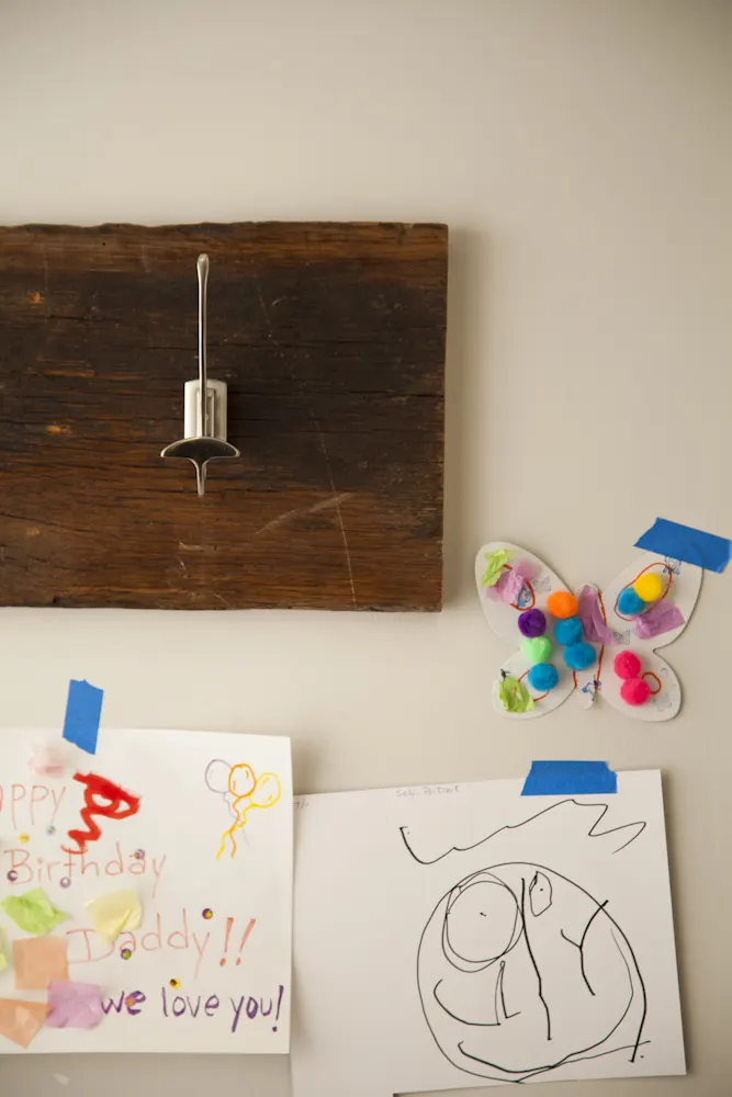 A steel hook on a reclaimed timber board, above children's drawings taped to the wall.