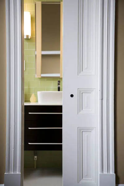 A black floating vanity with a white vessel basin against green glass tile, framed by white pilasters.